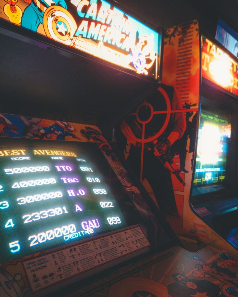 Row of retro arcade cabinets glowing at night. Photo by Lynn C on Unsplash.